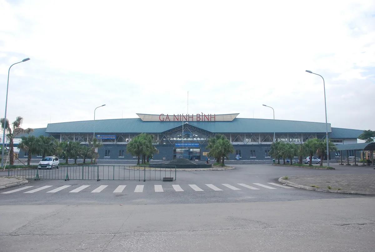 The Ninh Binh railway station building with a pale green roof and the sign GA NINH BINH, palm trees in the forecourt