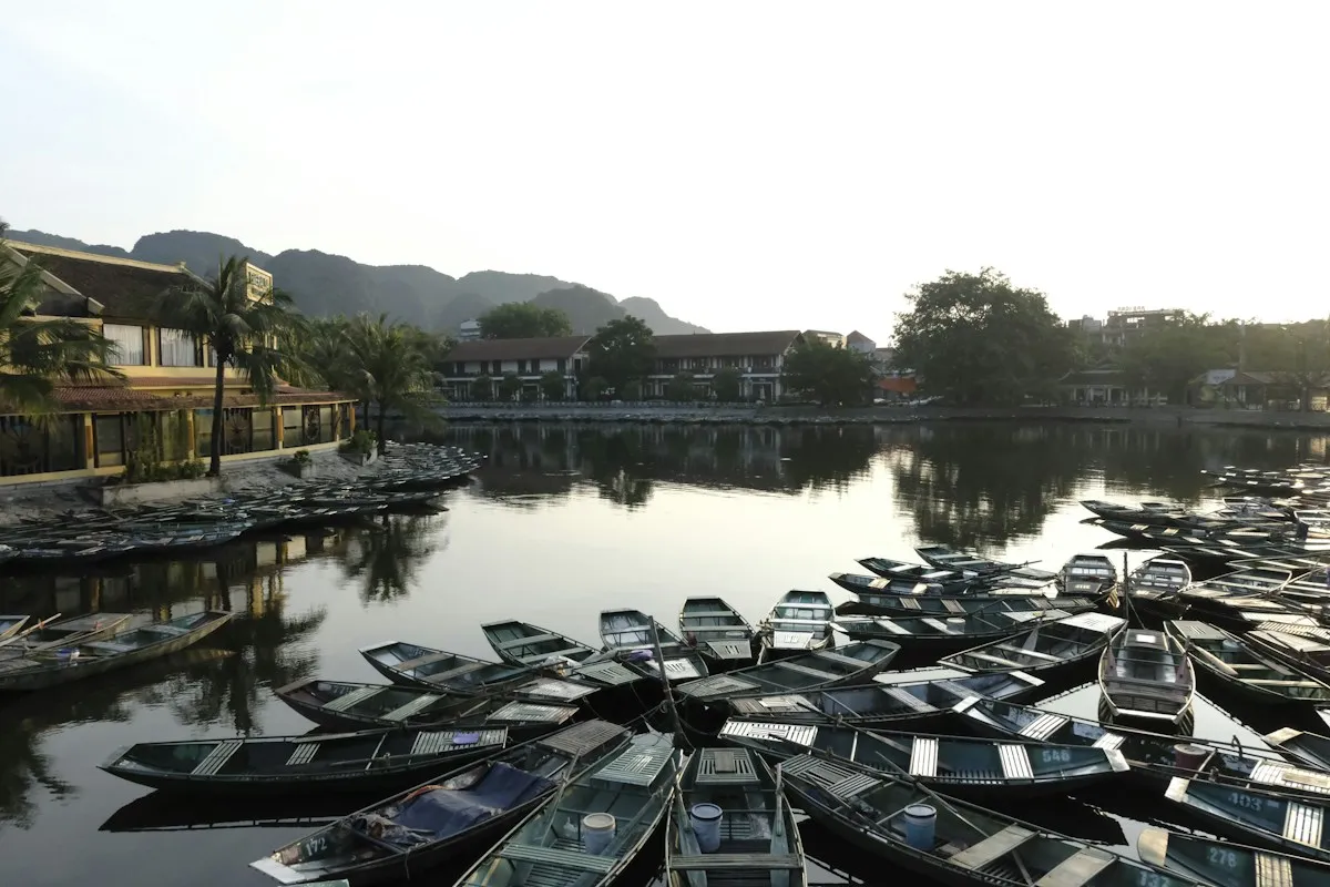Dozens of empty rowing boats moored together on still water at Tam Coc, with limestone hills behind