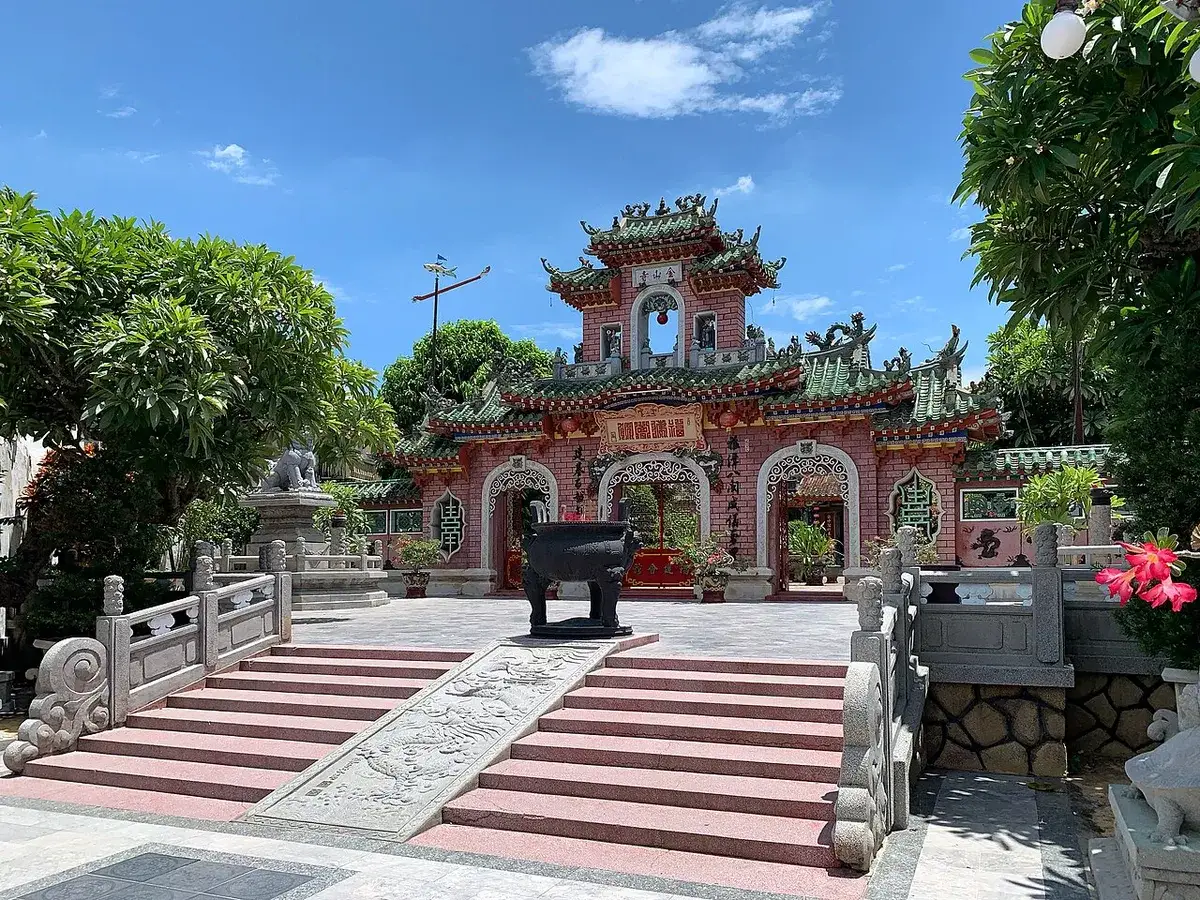 The pink triple-arched gate of the Fujian Assembly Hall in Hoi An, with an iron incense urn and stone steps in front