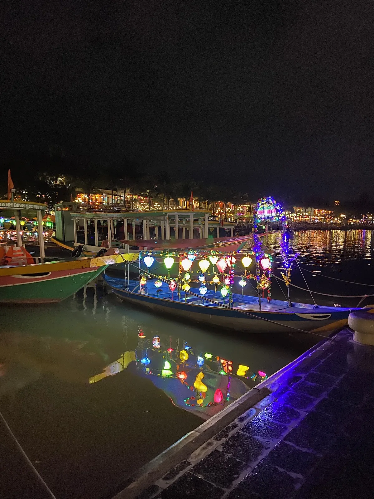 Wooden tourist boats strung with coloured lanterns moored on the Thu Bon River at night, their lights reflected in the water