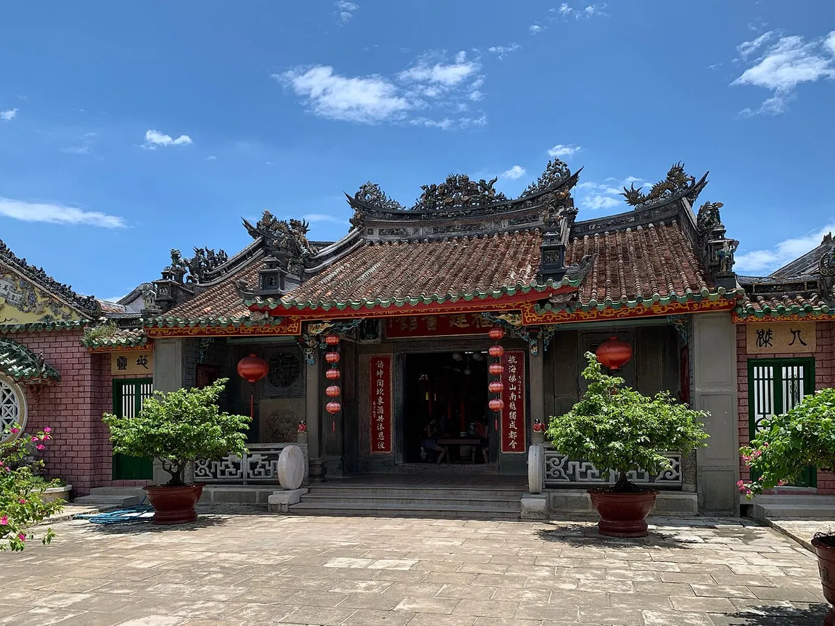 The tiled roof and red-lantern entrance of the Fujian Assembly Hall's main building in Hoi An under a blue sky