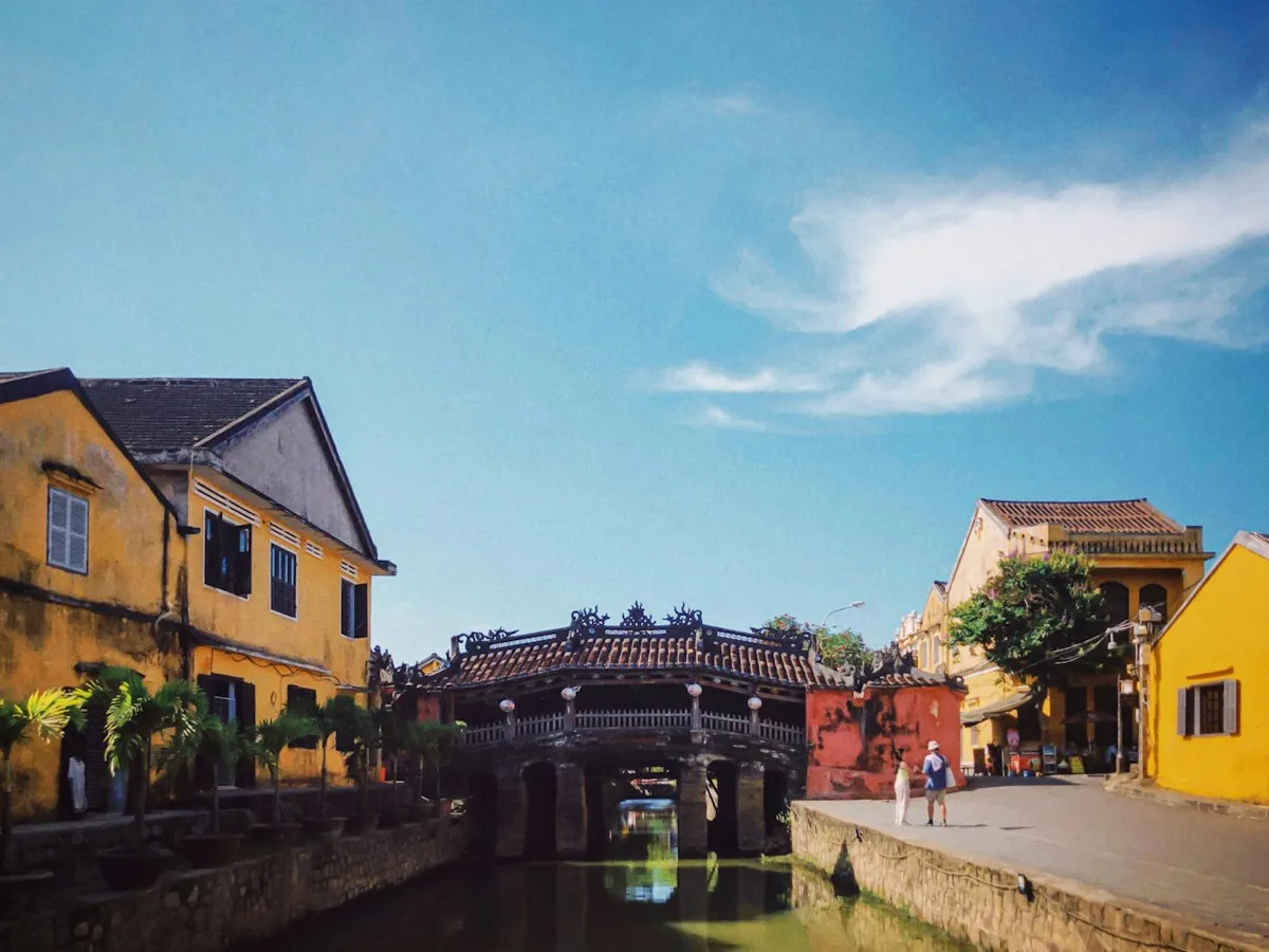 The Japanese Covered Bridge in Hoi An under a bright blue sky, framed by yellow houses beside a canal
