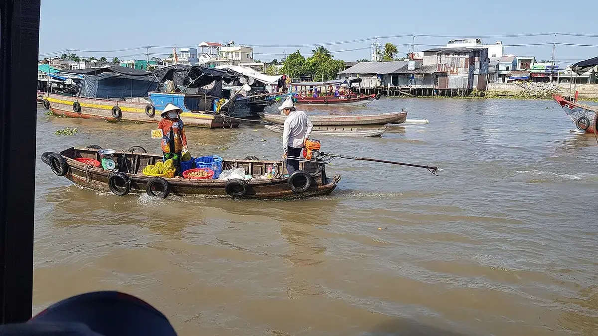 Vendors steering small wooden boats loaded with goods across the wide brown river at the Can Tho floating market