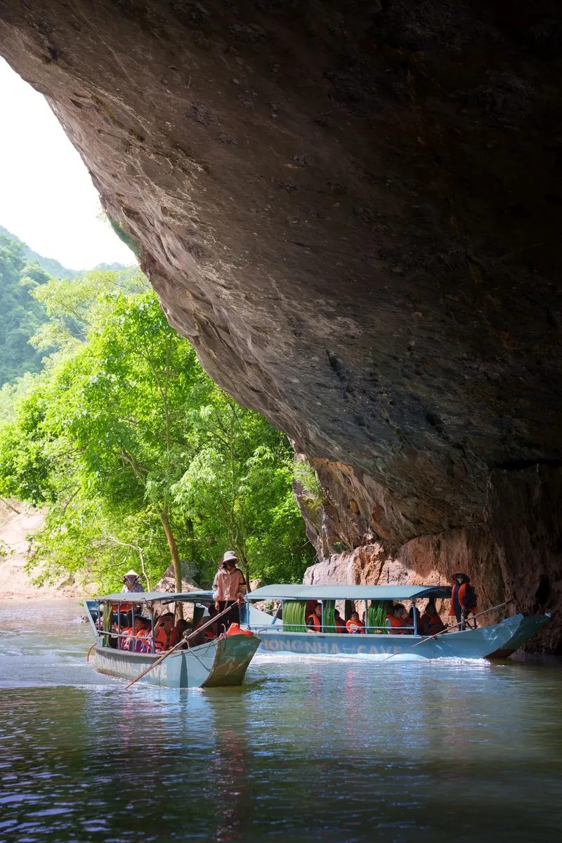 Two Phong Nha Cave boats full of passengers in orange life jackets rowed out under the cave mouth's rock overhang
