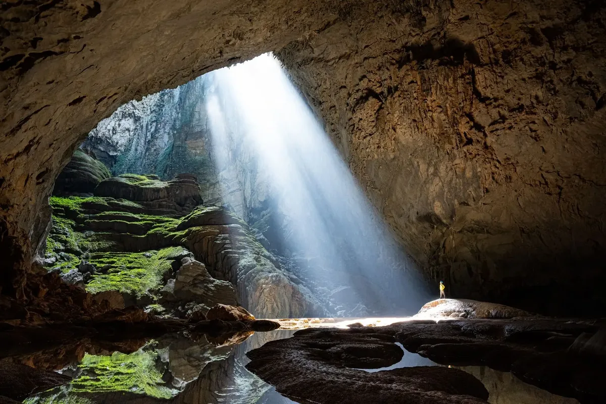 A beam of sunlight falling through the first doline into Son Doong cave, with a person standing in the light