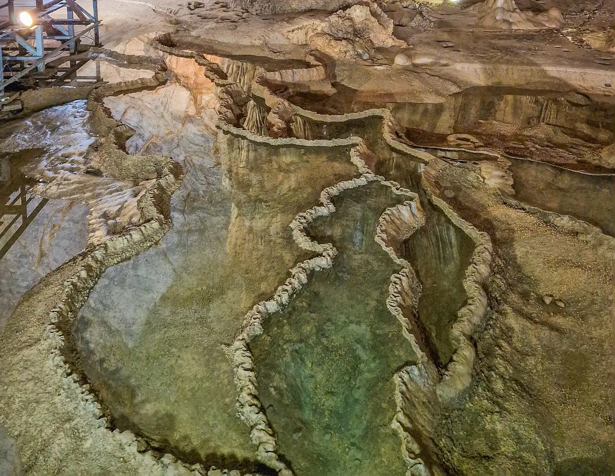 Stepped rimstone pools of still water beside a walkway railing inside Paradise Cave in Phong Nha-Ke Bang National Park