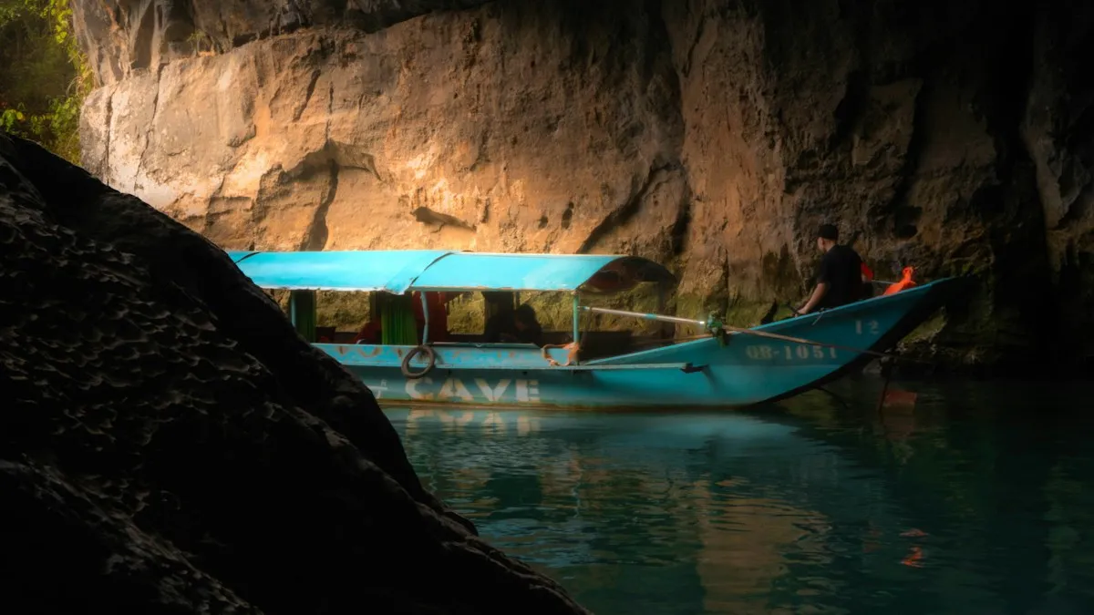 A boatman steering a blue Phong Nha tour boat through the dark limestone passage of the cave