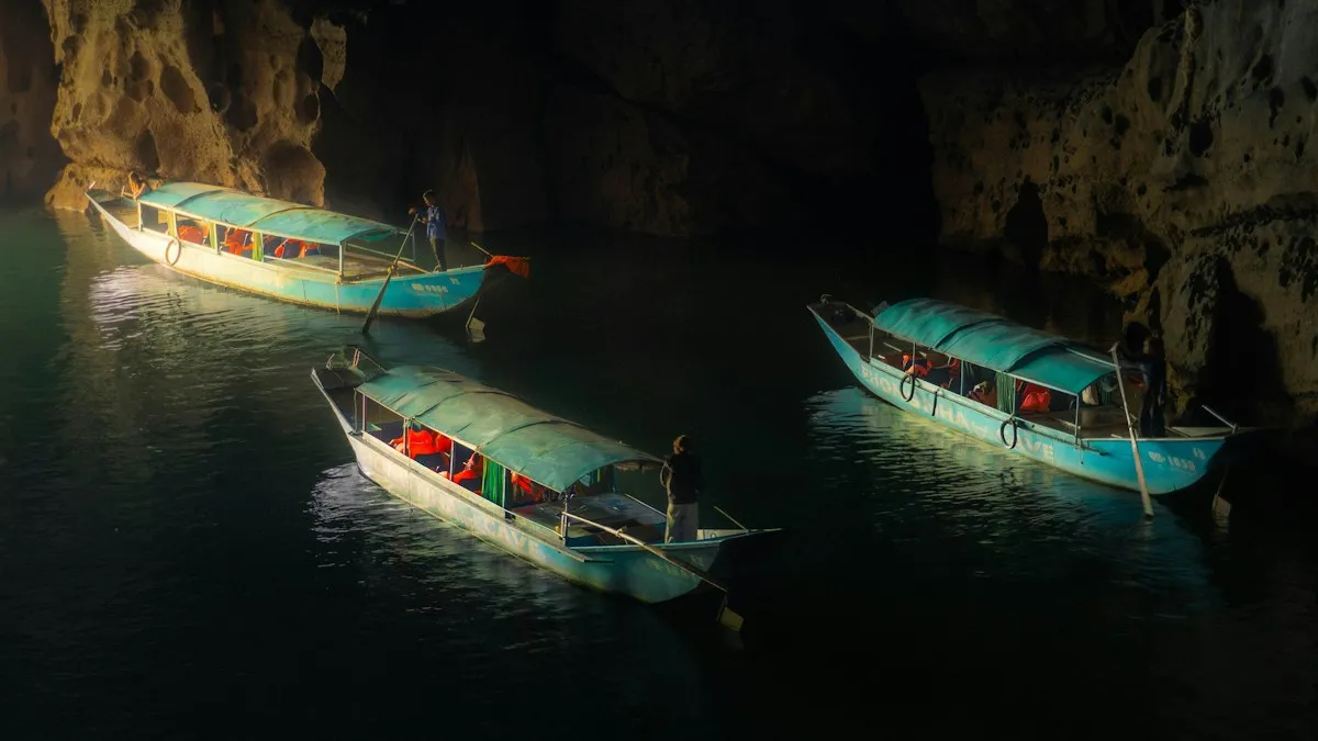 Three blue canopied tour boats with passengers gliding on the dark underground river inside Phong Nha Cave
