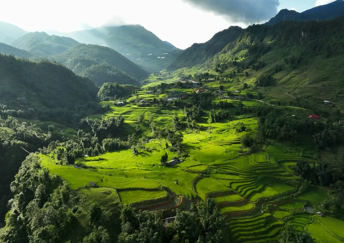 A lush green valley of rice terraces near Sa Pa from above, with forested ridges and low cloud on the peaks