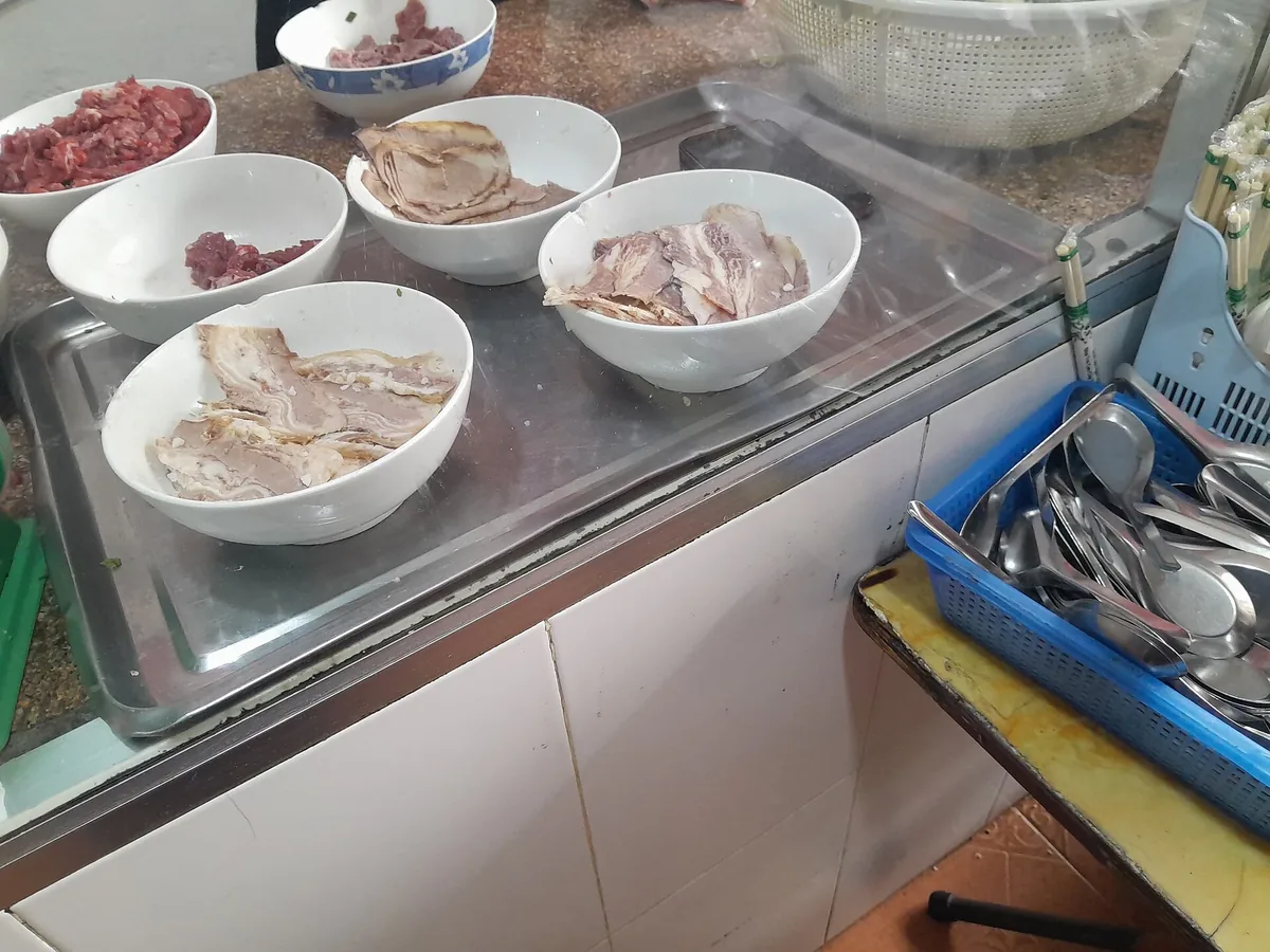 Bowls of sliced beef and raw beef laid out on the steel counter of a pho stall in Hanoi, ready for the broth