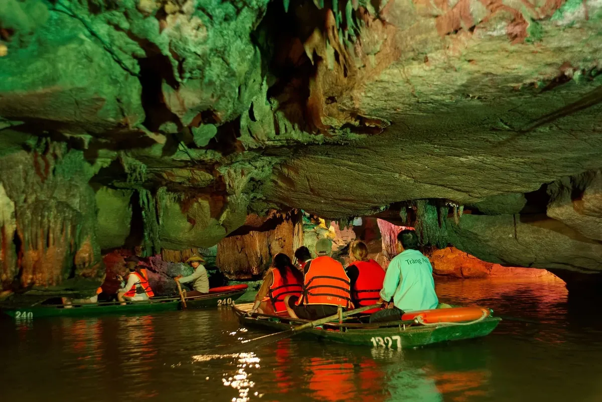 Visitors in rowing boats passing through a lit cave in the Trang An Landscape Complex