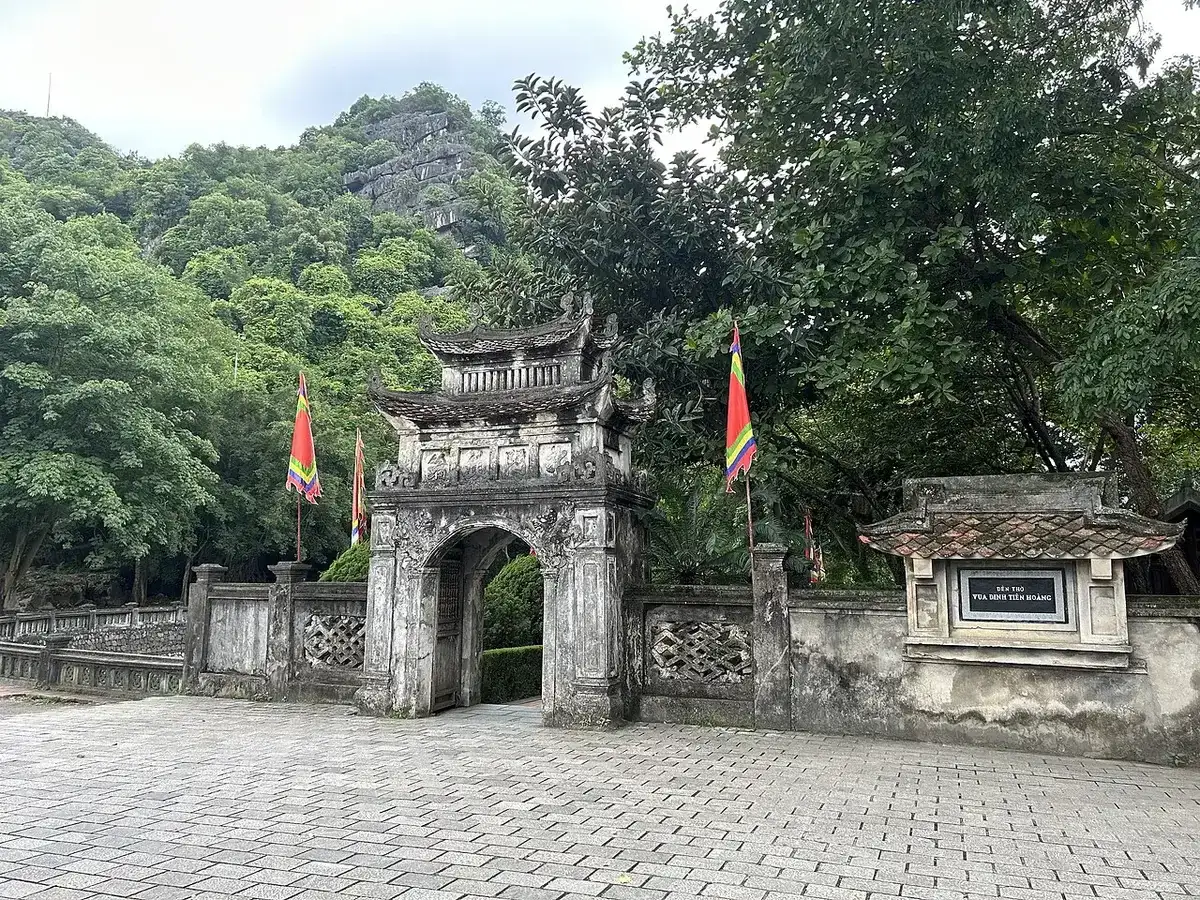 Stone gate of the temple of King Dinh Tien Hoang at Hoa Lu, with flags and a limestone hill behind