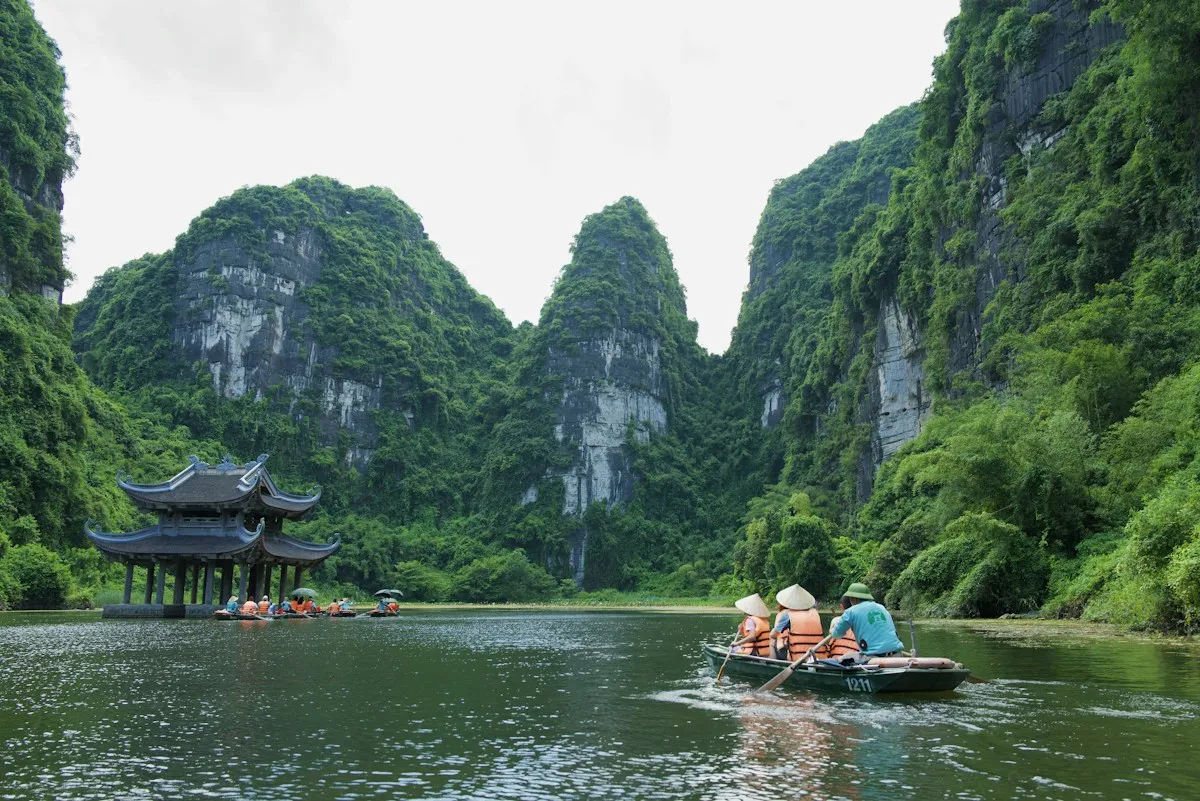 Rowers in conical hats taking visitors along the river at Trang An, a water pavilion below steep limestone cliffs