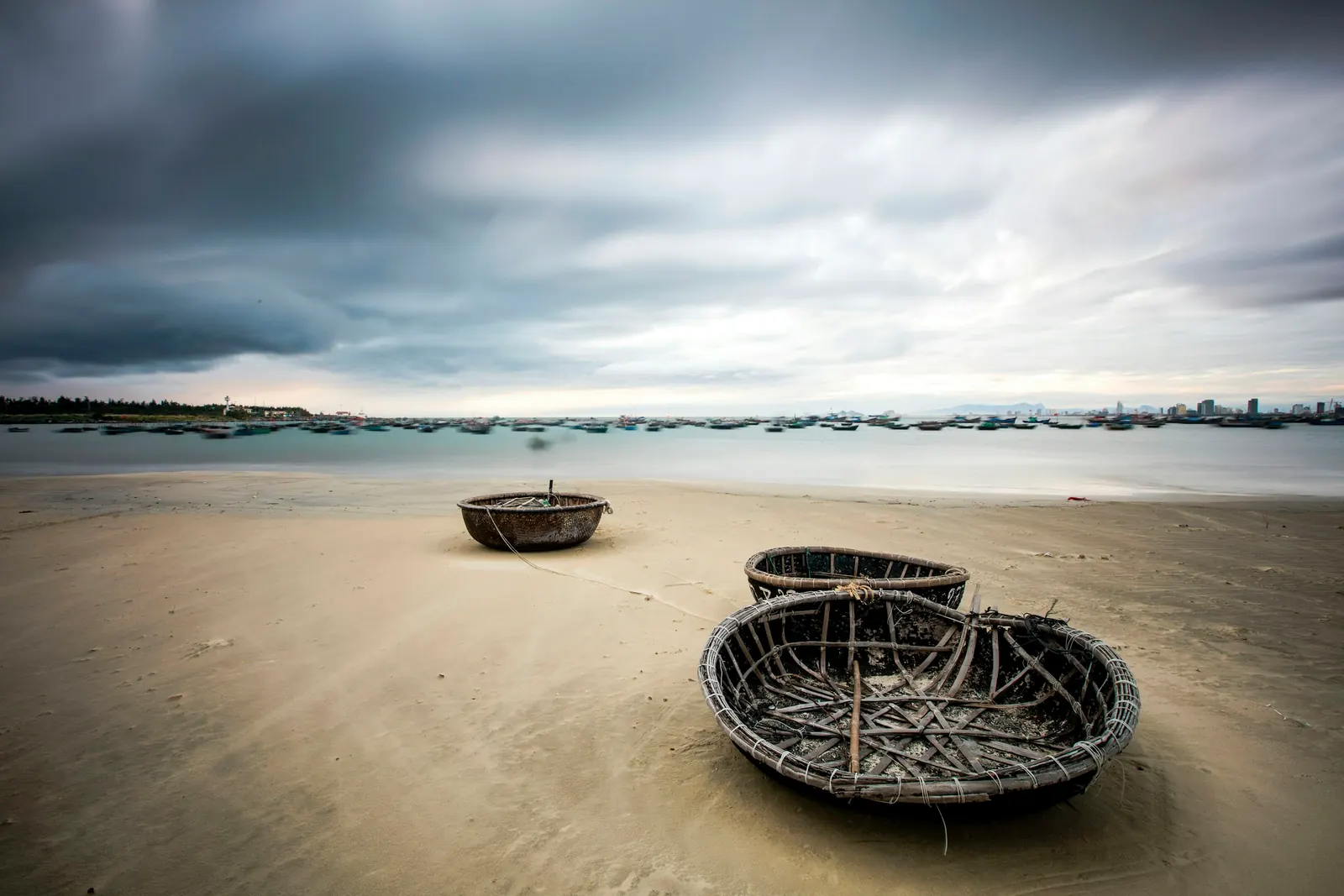 Round coracle boats on the sand under a cloudy sky