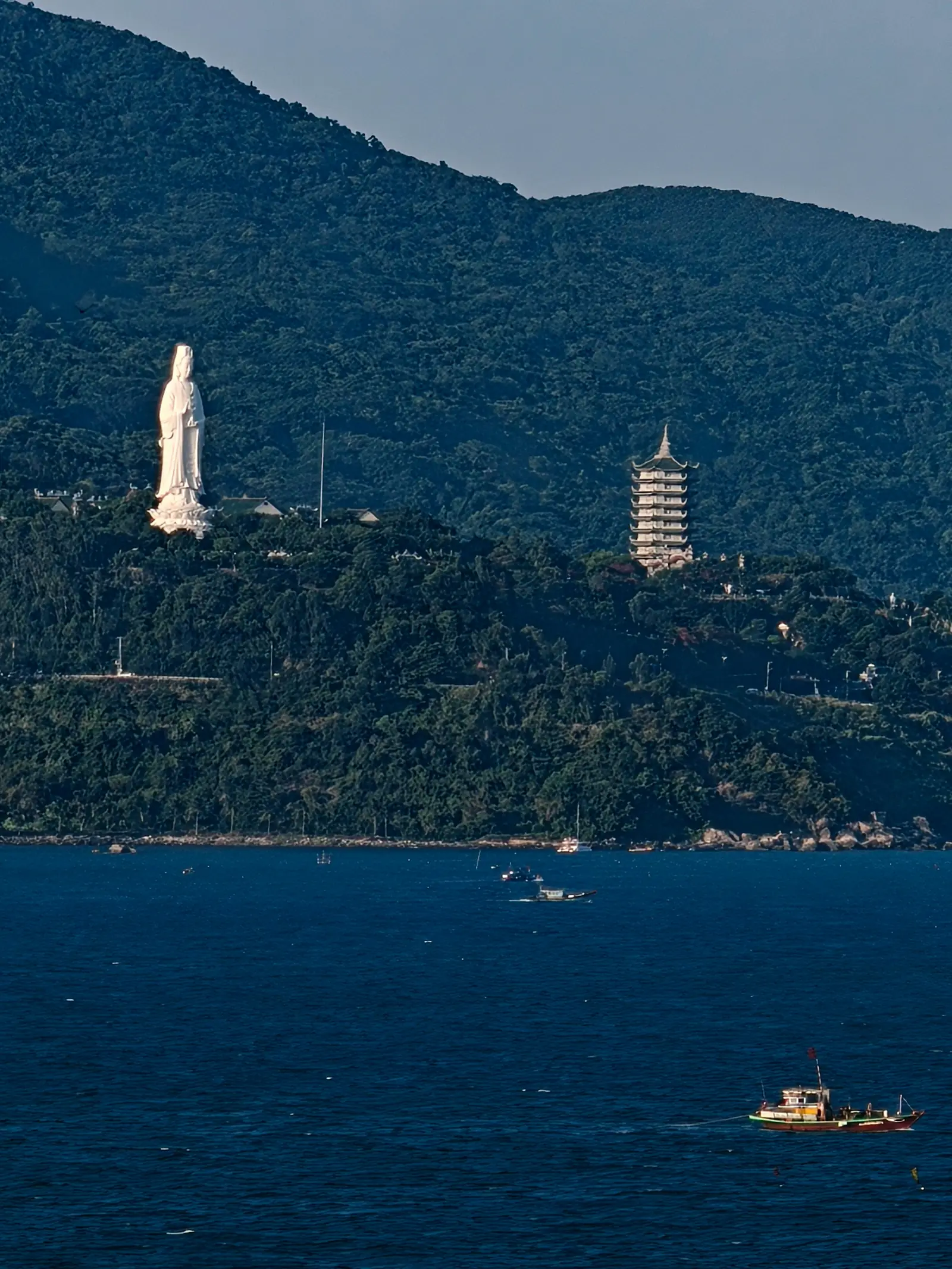 A white statue and a pagoda on the forested Son Tra peninsula above the sea