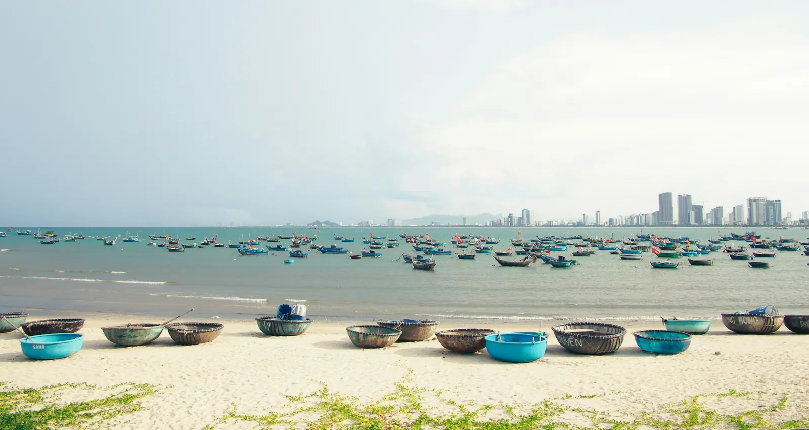 Boats lined up along the beach, the city skyline behind