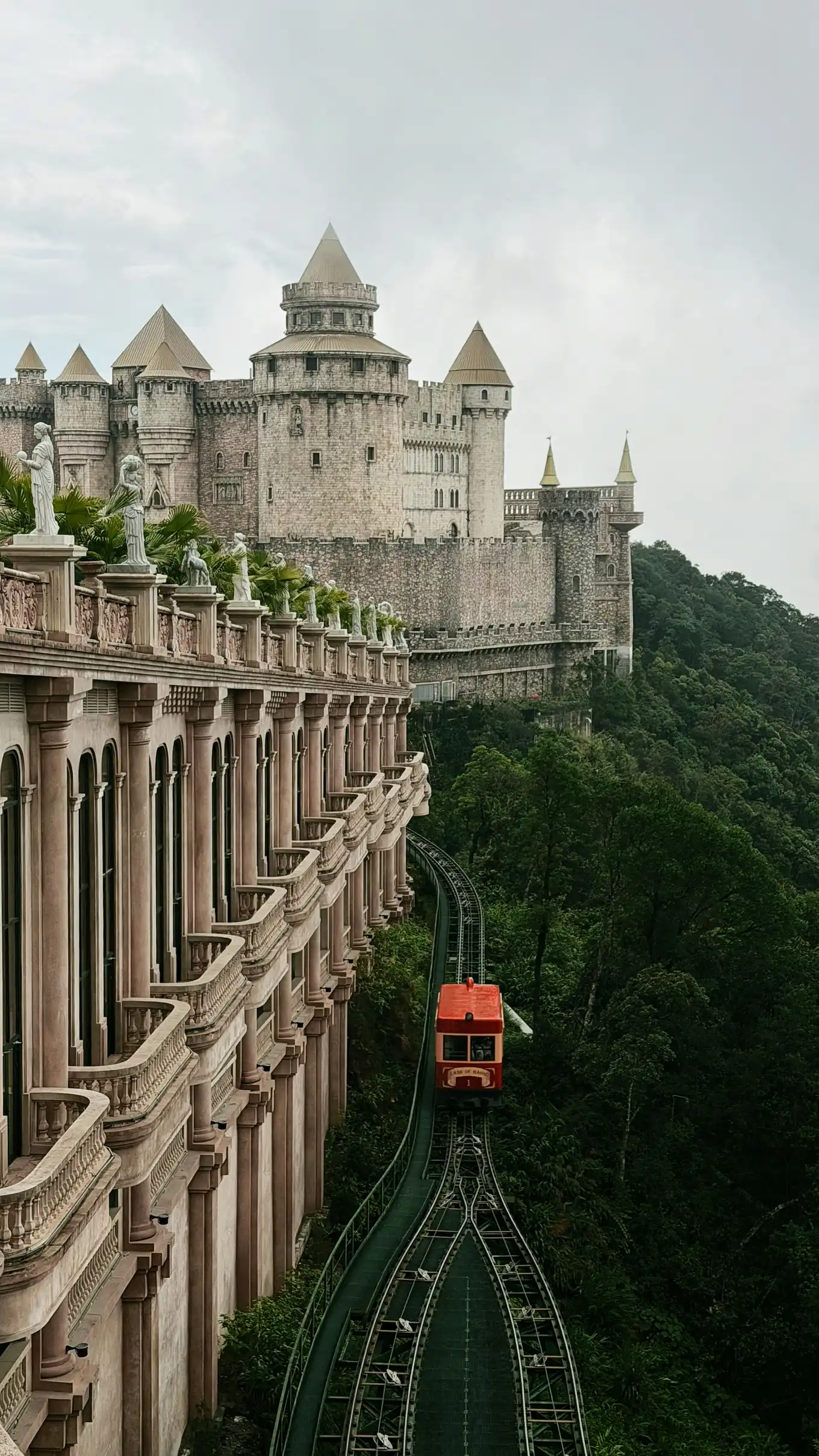 A red funicular train passing a stone castle on the forested slopes of Ba Na Hills