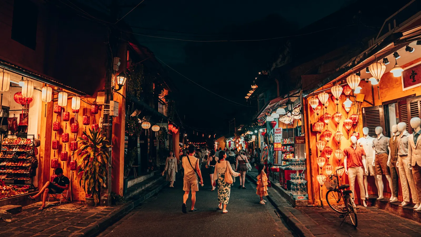 People walking down a narrow street lit by paper lanterns at night