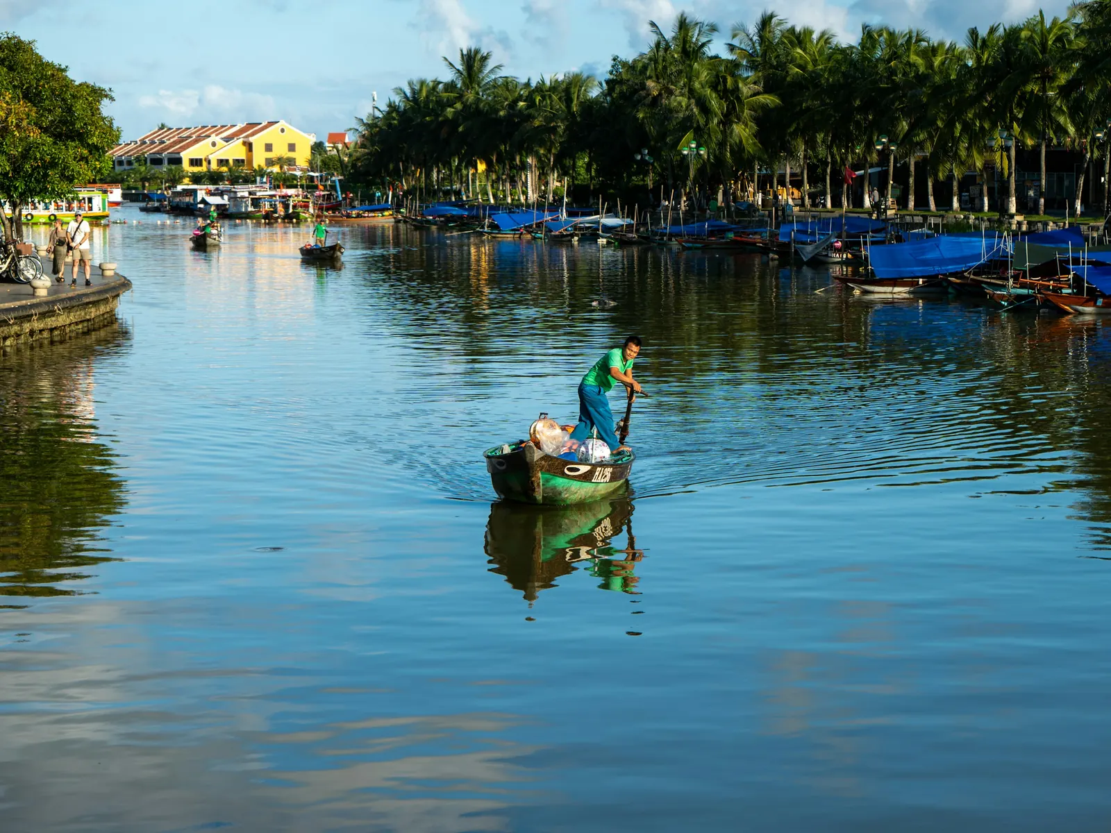 A man rows a boat loaded with goods on the calm river