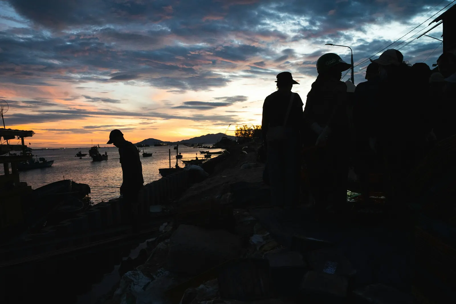 People silhouetted on the shore against an orange evening sky