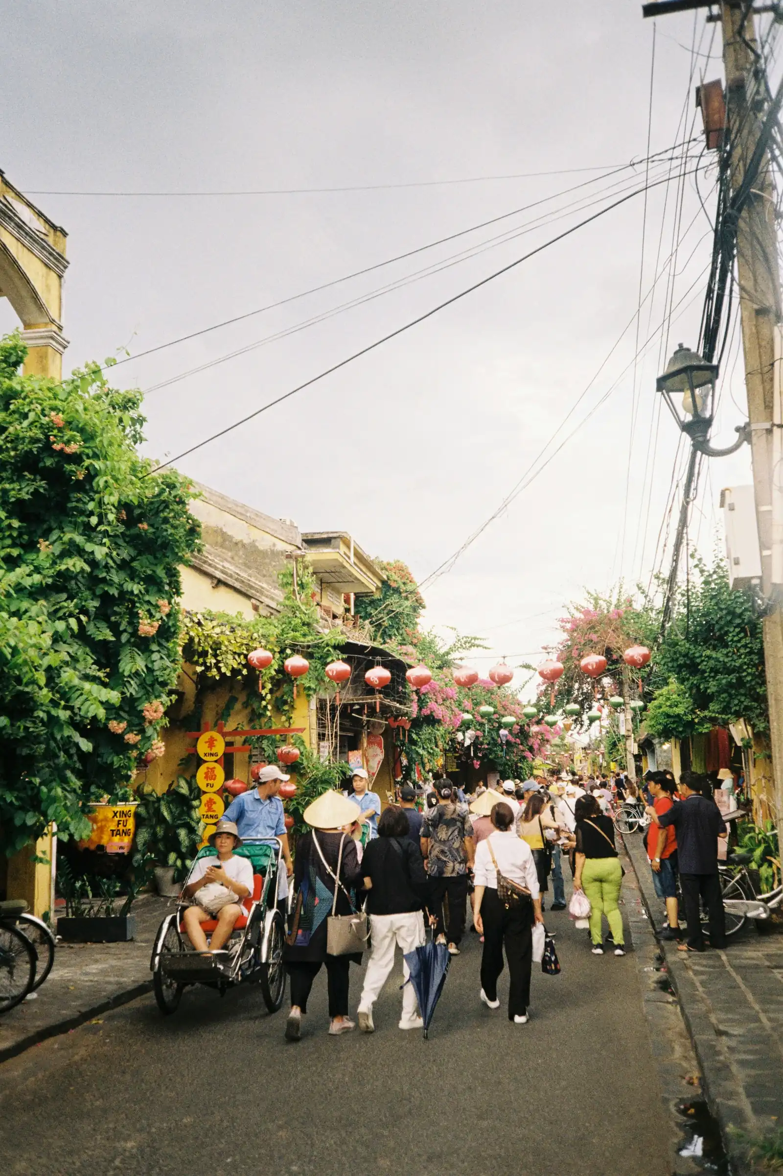 Pedestrians and a cycle rickshaw on a street hung with red lanterns