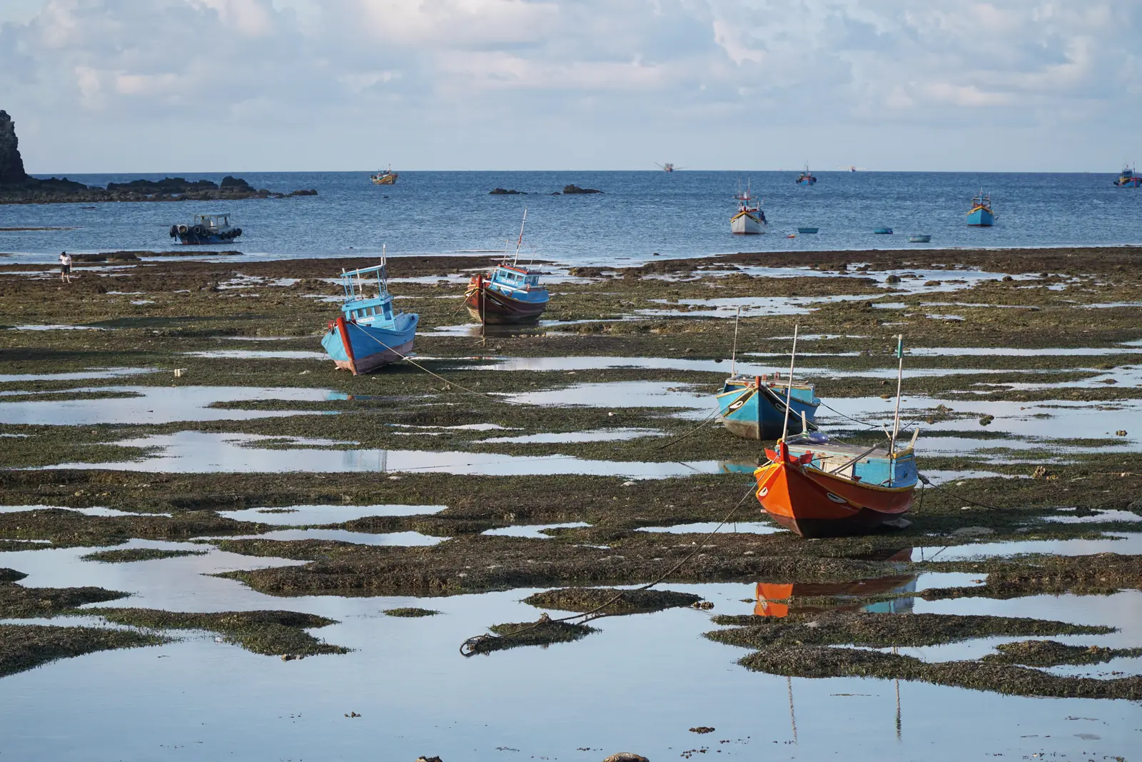 Fishing boats left on the reef flat at low tide on Phu Quy, with pools of seawater between the rocks
