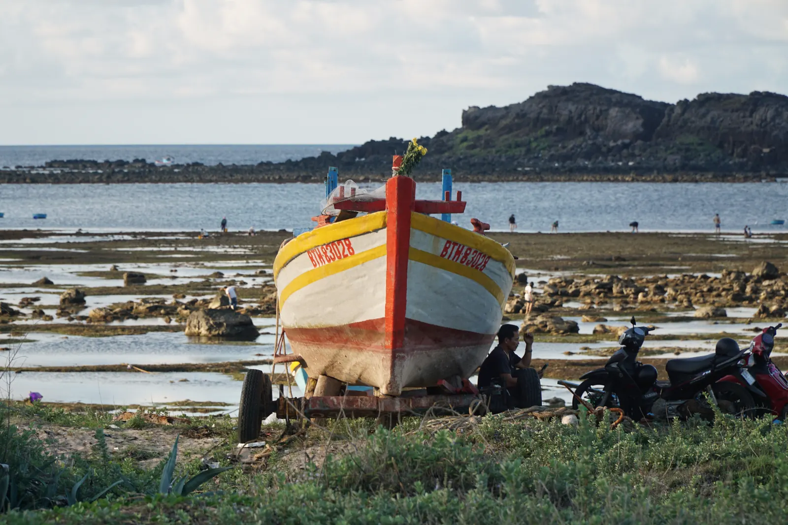 A red and yellow fishing boat on a trailer by the shore at low tide on Phu Quy