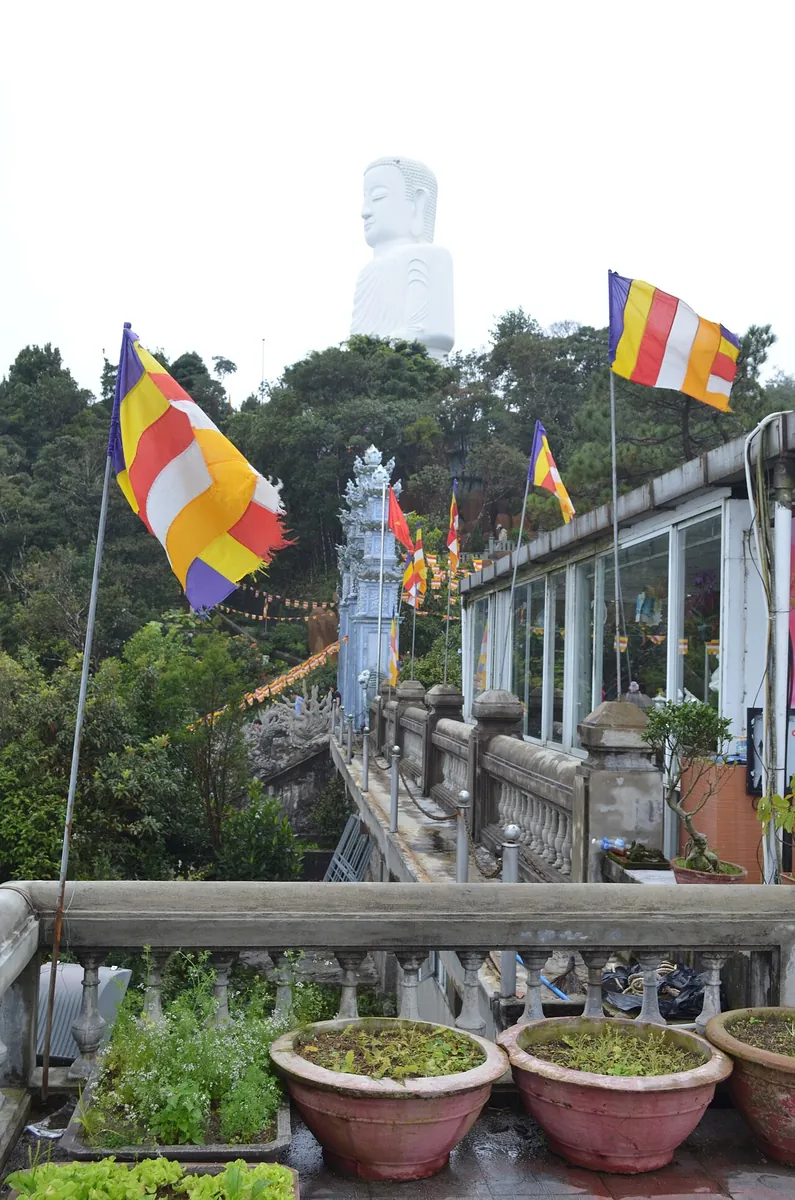 A Buddhist pagoda terrace at Ba Na Hills with prayer flags and a tall white Buddha statue on the hill above