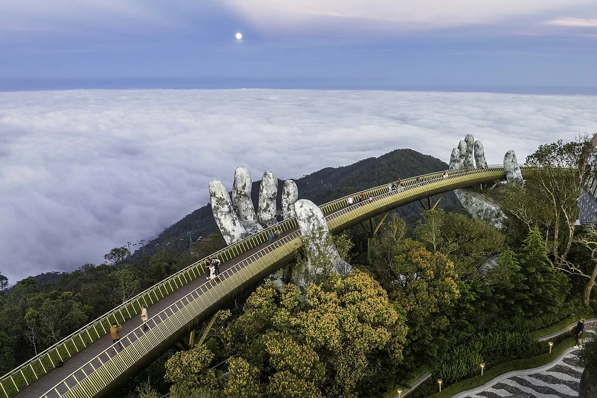 The Golden Bridge above a sea of cloud, held by two giant hands, with forested ridges below