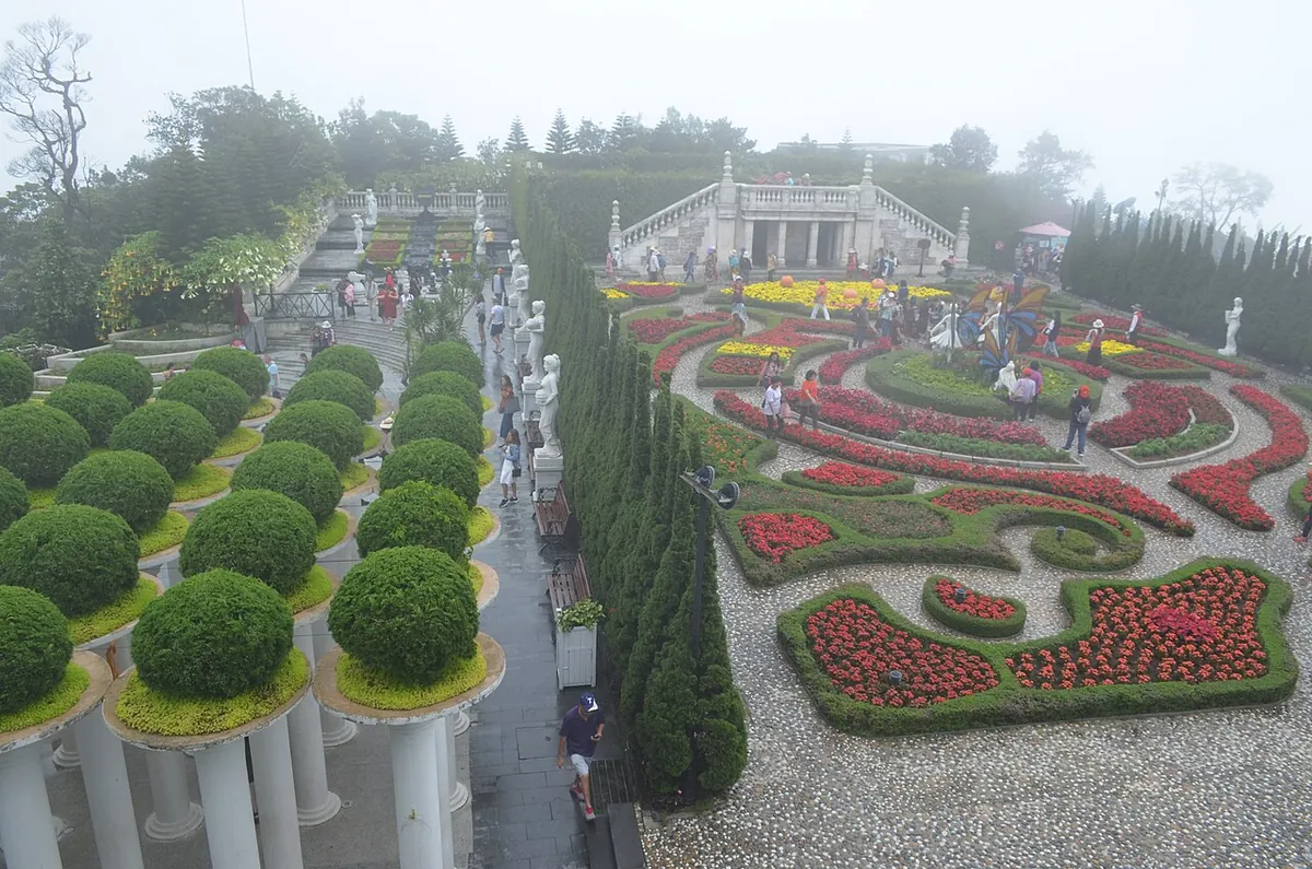 A formal flower garden on the summit of Ba Na Hills, with clipped trees and a colonnaded building in mist