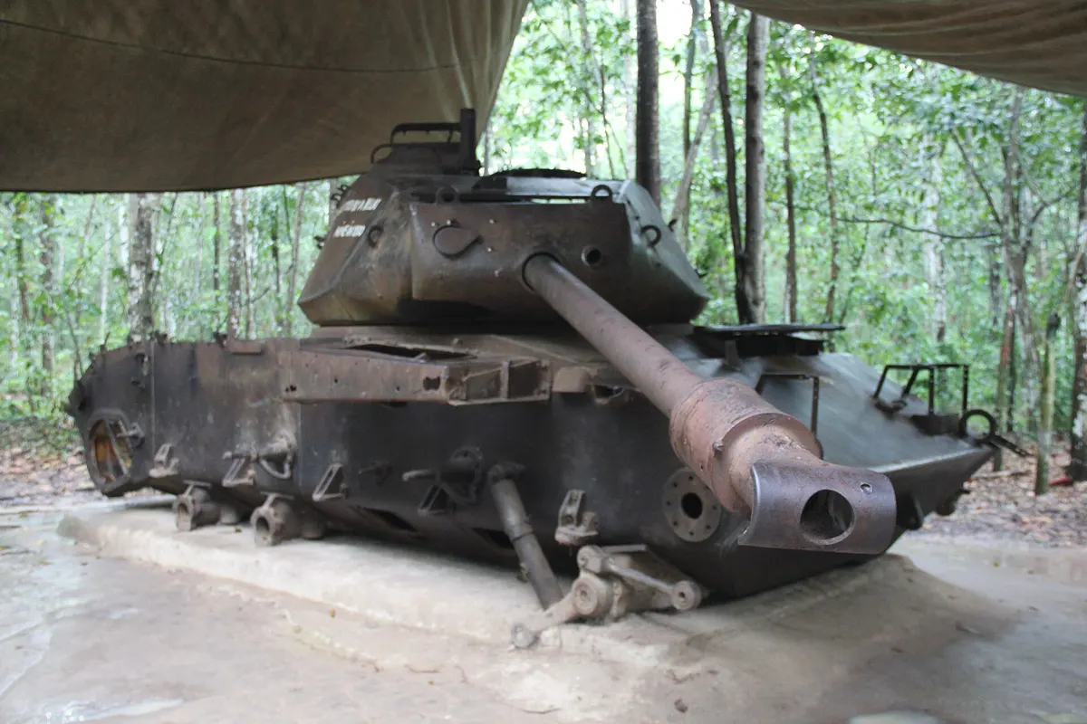 A rusted tank under a canvas shelter at the edge of the forest