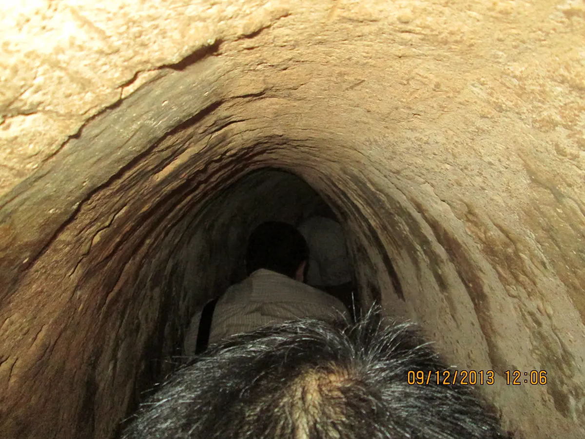 A narrow tunnel with rounded earth walls, a visitor crouching ahead of the camera