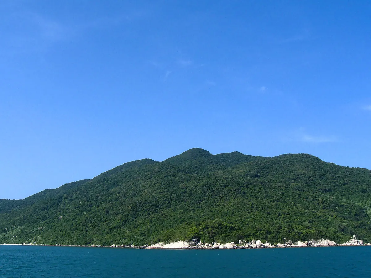 The green, forested ridge of one of the Cham Islands rising from deep blue sea under a clear sky