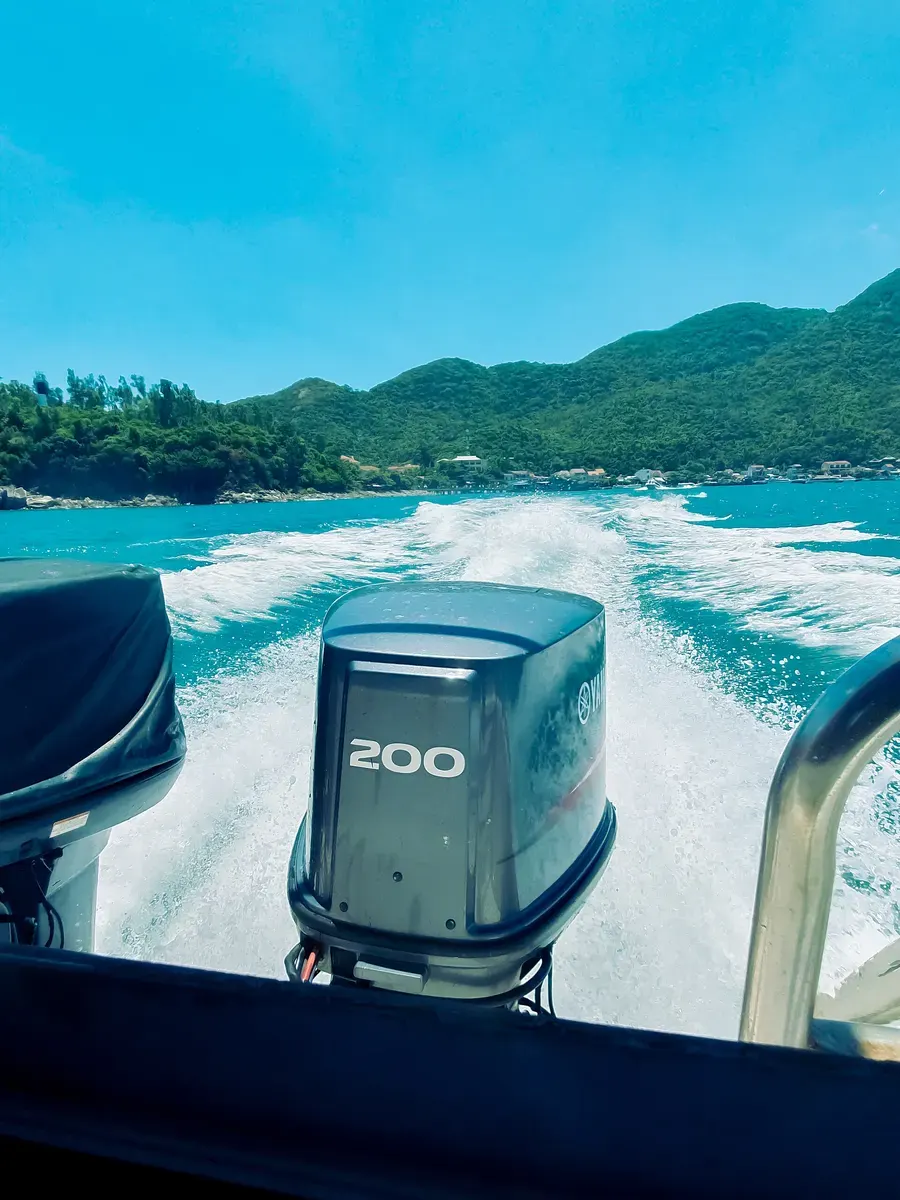 The wake of a speedboat with a large outboard motor, heading away from a green island with houses along the shore