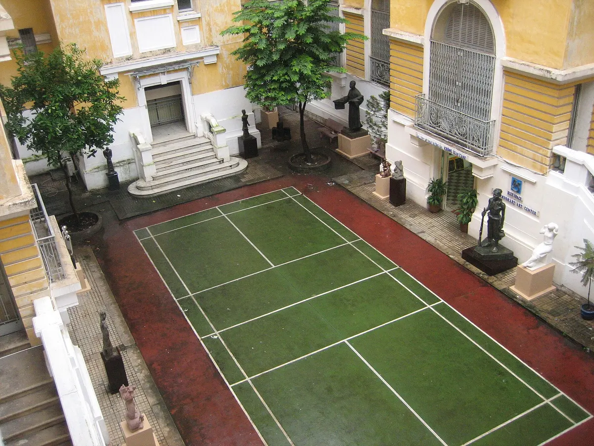 A courtyard seen from above, with a green sports court in the middle and bronze statues along the walls