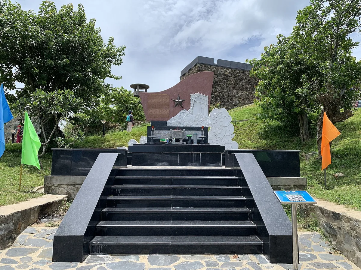Black granite steps leading up to a memorial and the stone walls of Hai Van Gate, with flags on the grass