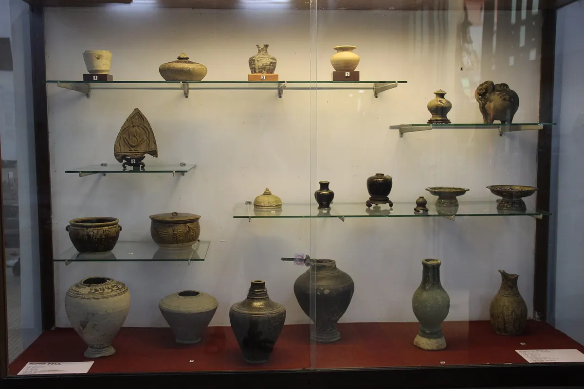A glass case of old glazed jars, bowls and pots on several shelves