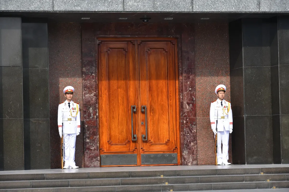 Two honour guards in white uniforms standing either side of the mausoleum's tall wooden doors