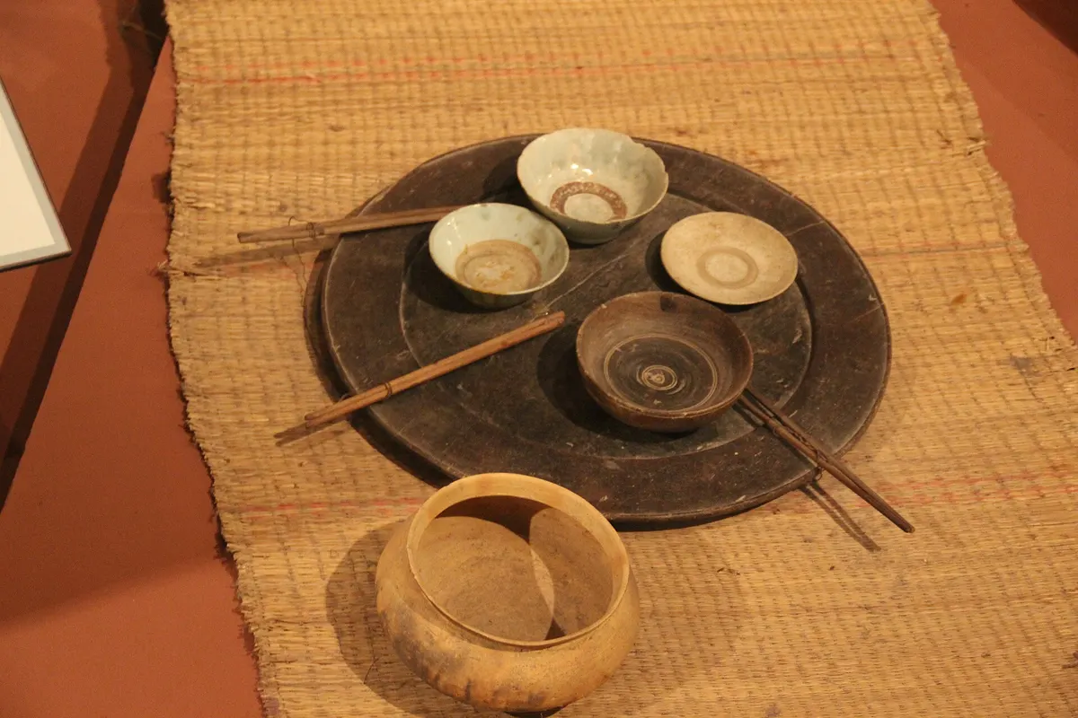 A museum display of a woven mat with bowls and chopsticks set on a round tray