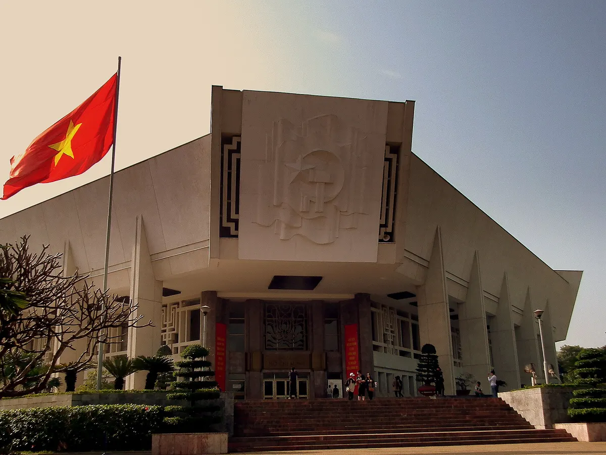 The museum's angular white facade seen from the steps, with a red flag and trimmed shrubs in front