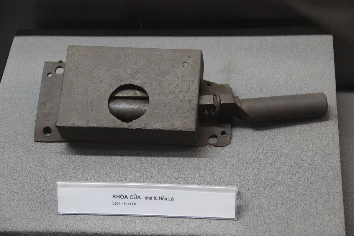 A heavy iron lock with a sliding bolt, displayed in a case at Hoa Lo Prison