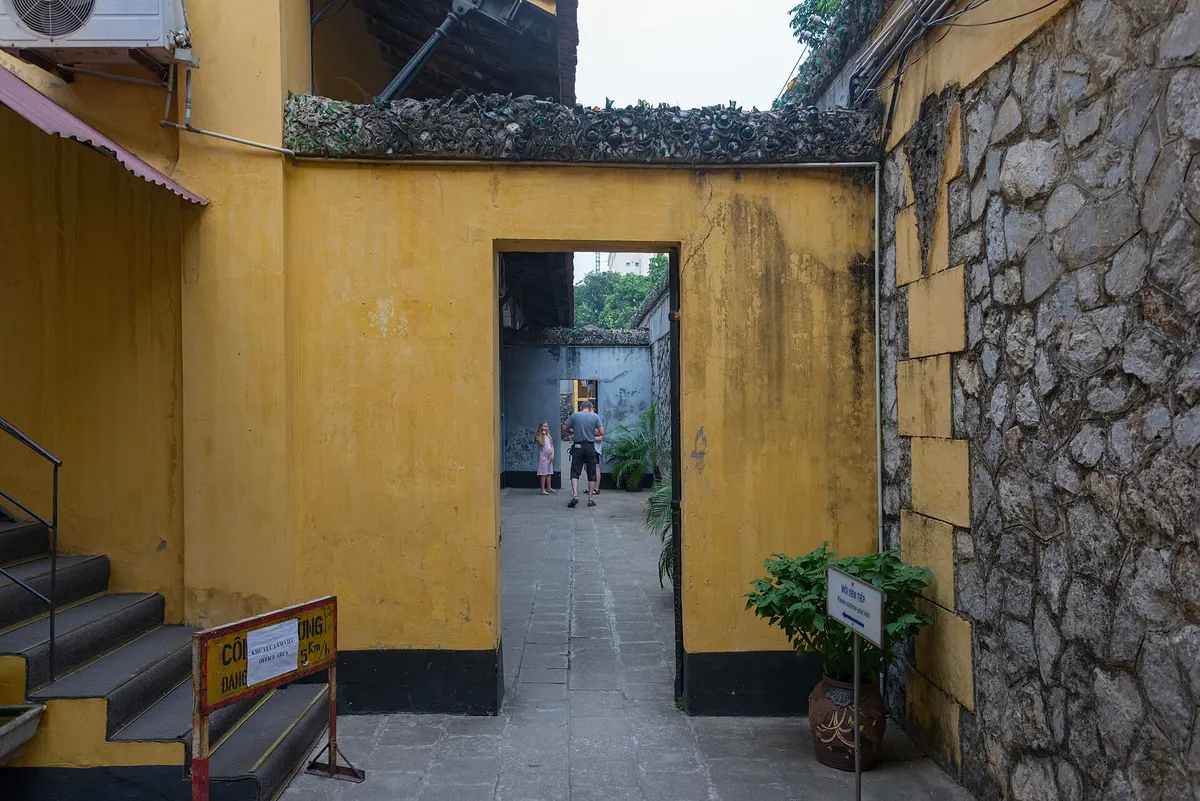 A narrow yellow-walled courtyard inside Hoa Lo Prison, with a doorway leading through to another yard