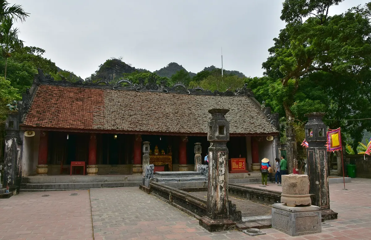 A low tiled-roof temple hall at Hoa Lu behind a paved courtyard with stone pillars and an incense burner