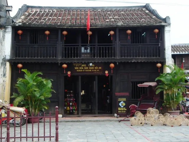 The front of the Hoi An Museum of Folk Culture, a long two-storey building with a dark tiled roof, red lanterns and a wooden balcony