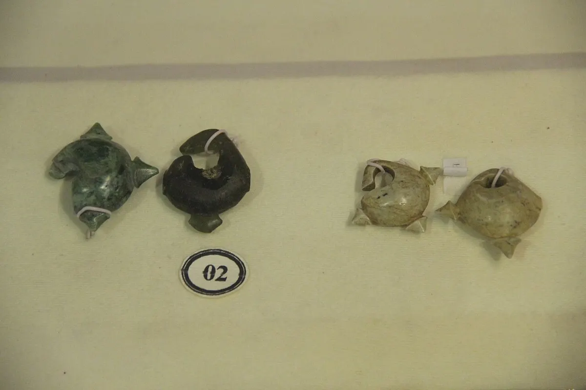 Four small bronze and stone ear ornaments laid out in a museum display case with a numbered label