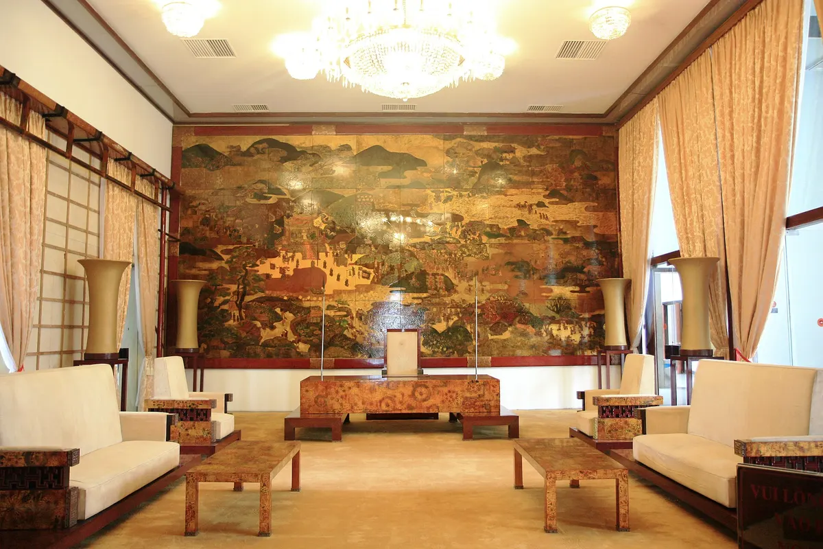 A reception room with cream sofas, a low table and a huge lacquer painting covering the back wall