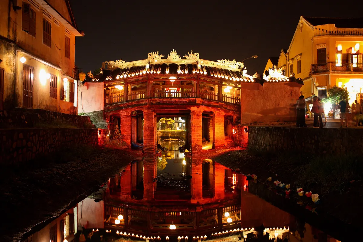 The covered bridge at night before the restoration, lit red and reflected in the water of the creek