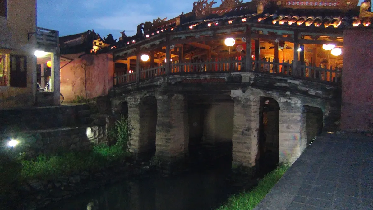 Side view of the covered bridge at dusk, showing the stone piers and the roofed wooden gallery above