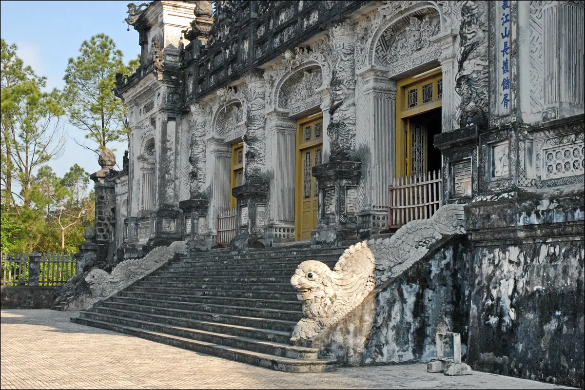 The entrance to the tomb's main hall, a grey facade of carved pillars and arched windows behind a stone dragon on the stairs