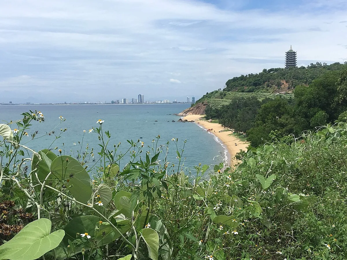 View from Son Tra over a curving beach and the sea toward the high-rises of Da Nang, with the pagoda's tower on the headland